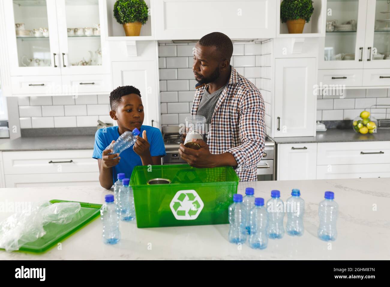 Joyeux père et fils afro-américains en cuisine parlant et triant les déchets plastiques pour le recyclage Banque D'Images