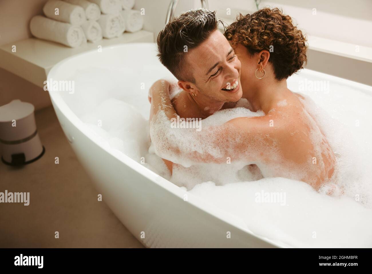 Un jeune couple de queer souriant appréciant un bain moussant ensemble. Jeune couple romantique s'amusant ensemble dans la baignoire à la maison. Jeune LGBTQ+ couple spen Banque D'Images