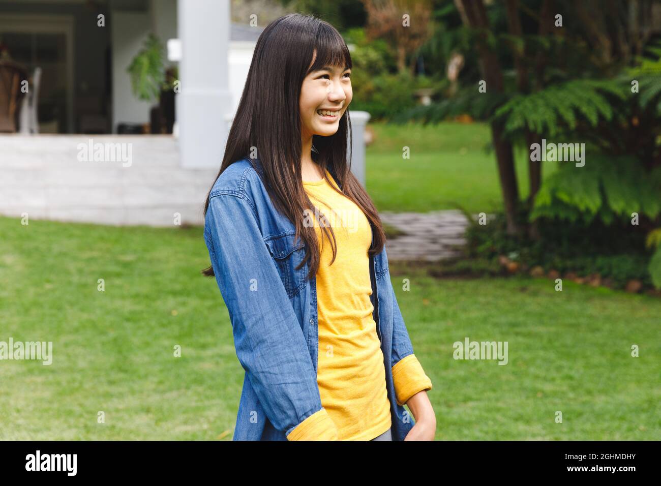 Bonne fille asiatique souriant dehors dans le jardin à l'extérieur de la maison de famille portant des vêtements décontractés Banque D'Images