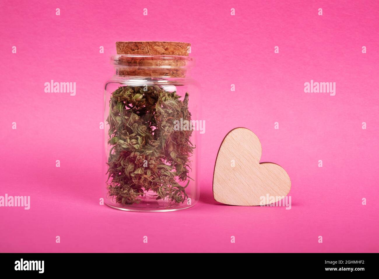symbole de l'amour de la marijuana, pot avec des bourgeons secs de cannabis et un coeur en bois sur fond rose. Banque D'Images