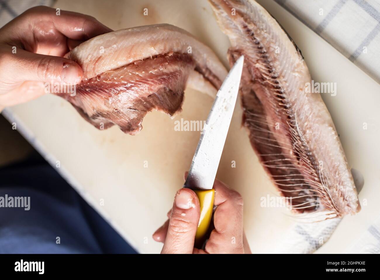 Les mains des femelles coupent le hareng salé à l'aide d'un couteau et séparent la chair des os, sur une planche à découper. Processus de cuisson. Vue de dessus. Banque D'Images