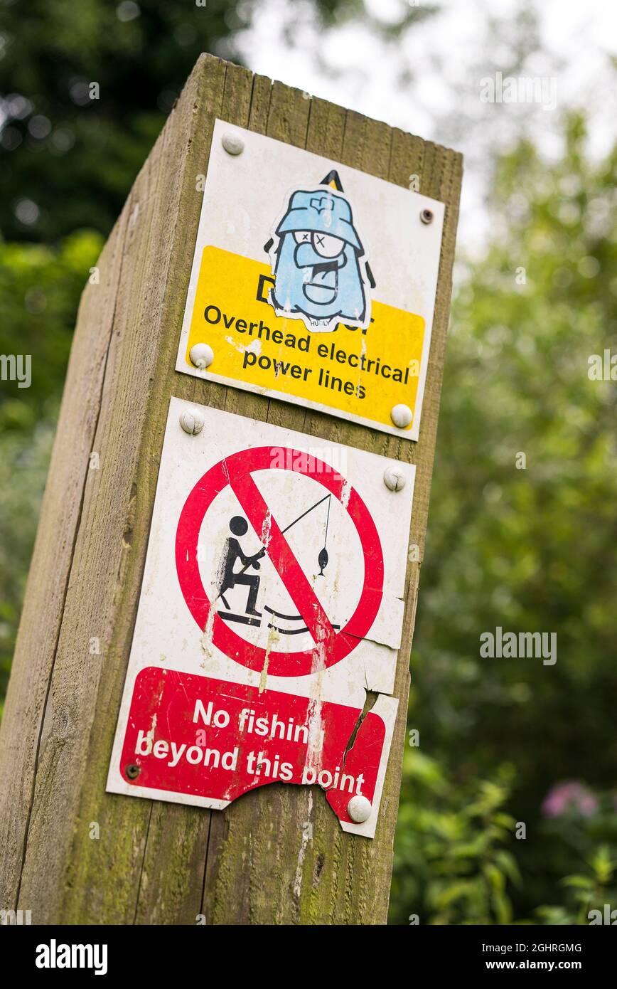 Panneau vandalisé pour les pêcheurs à la ligne sur poste extérieur avertissement de l'absence de pêche au-delà de ce point et danger dû aux lignes électriques aériennes. Banque D'Images