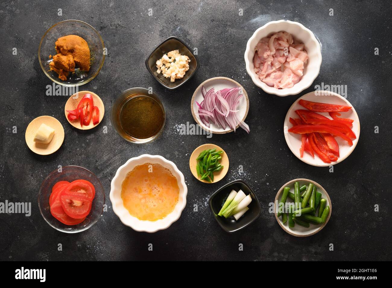 De nombreux ingrédients thaïlandais pour le plat de gaï pageli paggali avec poulet, oeufs, épicé, pâte de curry thaï jaune, tomate, riz dans un bol noir fait au wok. Traditionnel Banque D'Images