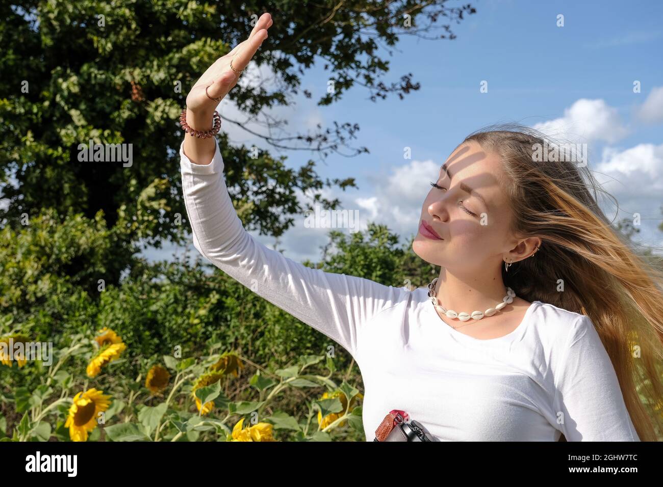 Belle adolescente debout dans un champ de tournesol en protégeant ses yeux du soleil, France Banque D'Images