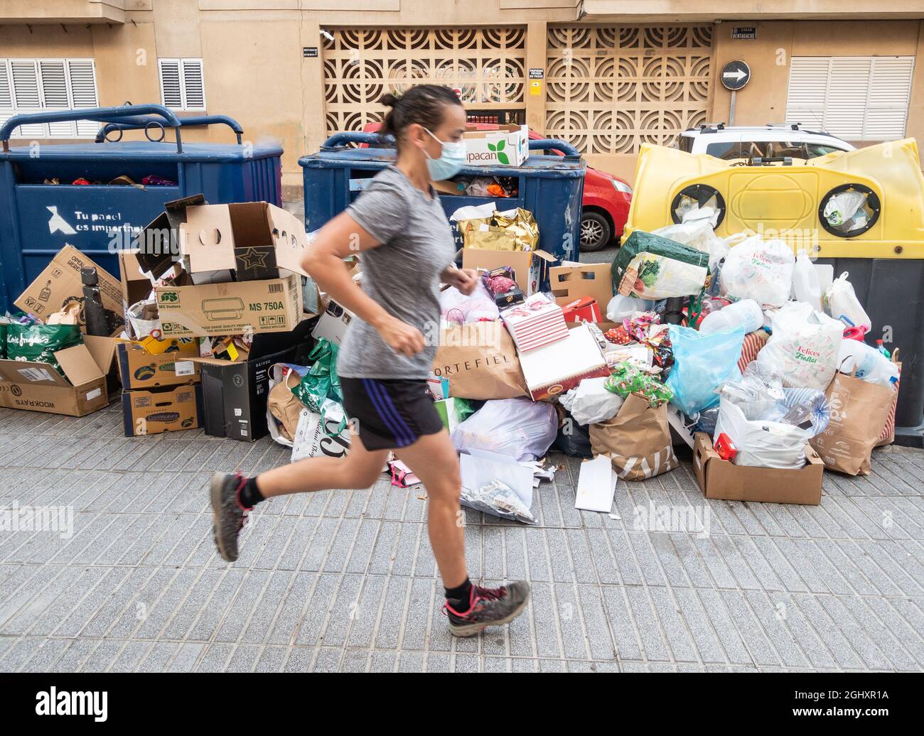 Jogging féminin passant devant des poubelles entassées à côté de conteneurs de recyclage communautaires complets dans la rue en Espagne Banque D'Images