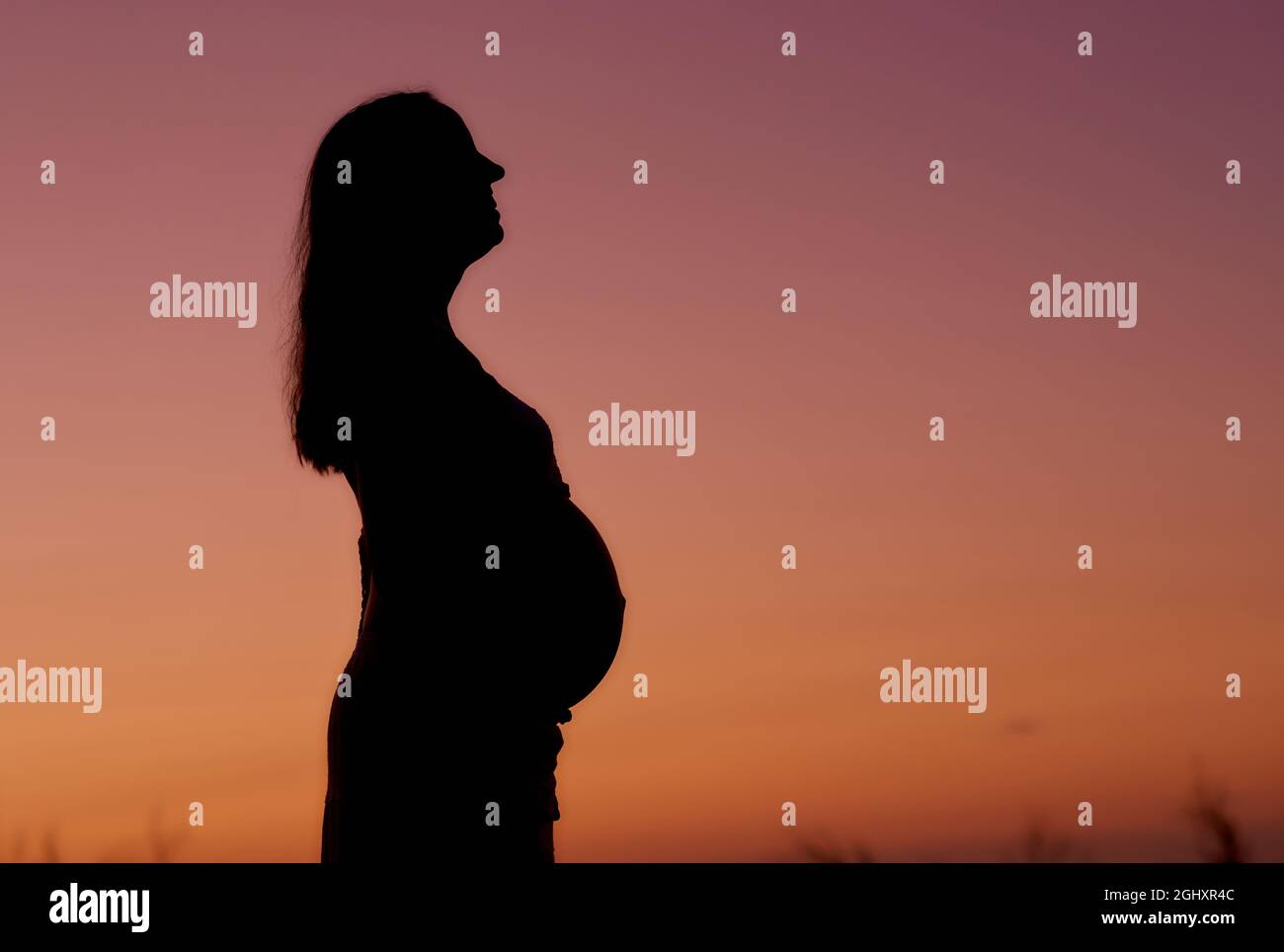 Femme enceinte contre le ciel du coucher du soleil Banque D'Images