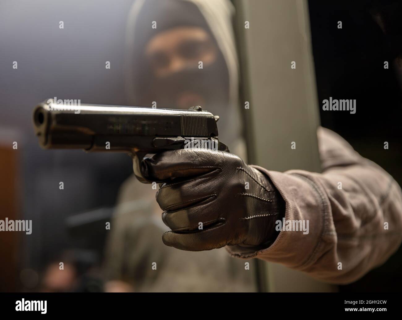 Criminel avec balaclava, attaque derrière le concept de fenêtre. Homme en noir capuche gris tient le pistolet dans la main gantée en cuir. Blur masqué armé tueur ro Banque D'Images