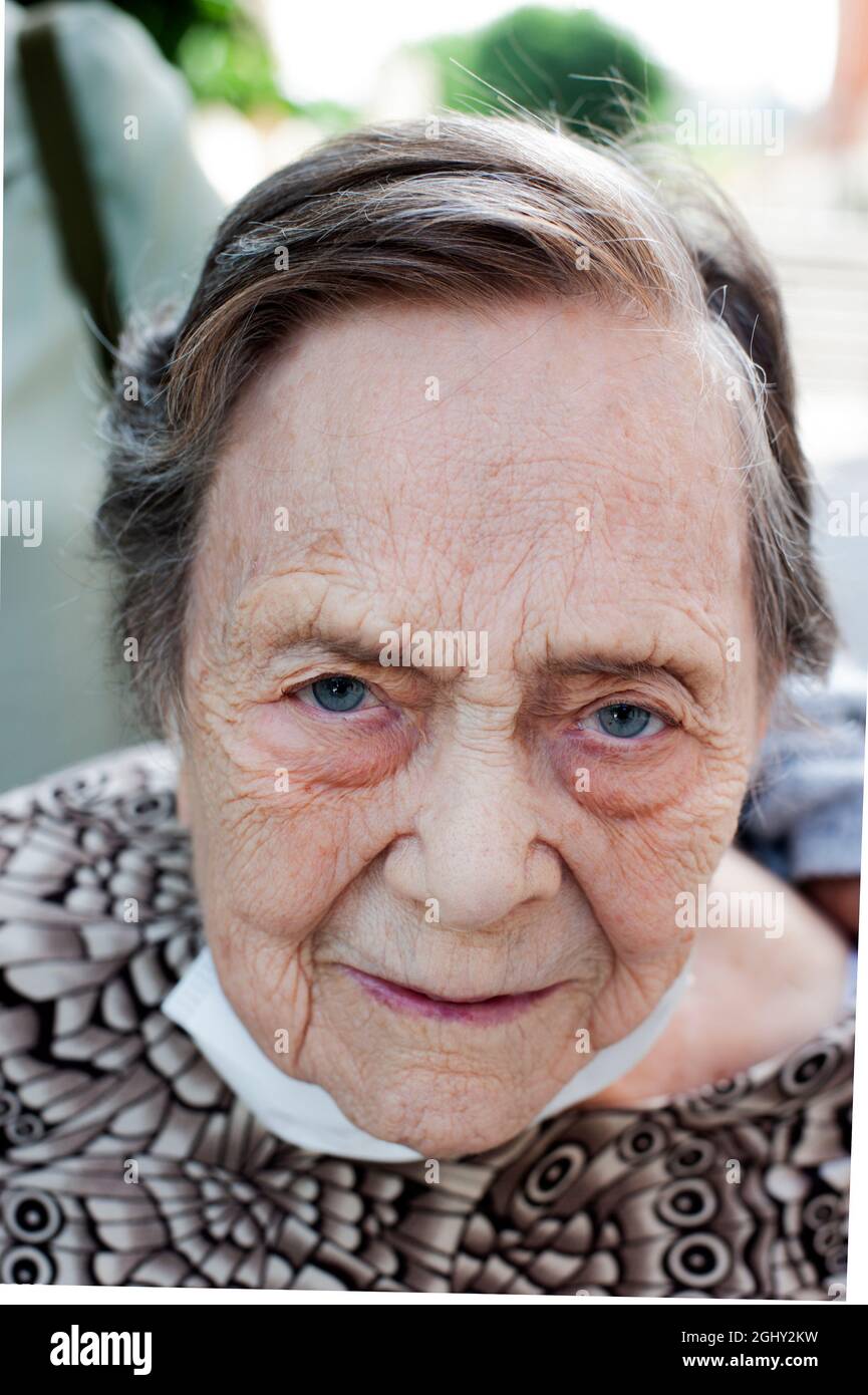 Gros plan d'une femme de plus de 80 ans souriant avec un masque protecteur vers le bas. Visage avec rides d'âge et yeux bleu-gris. Porter une chemise imprimée. Vieillesse Banque D'Images
