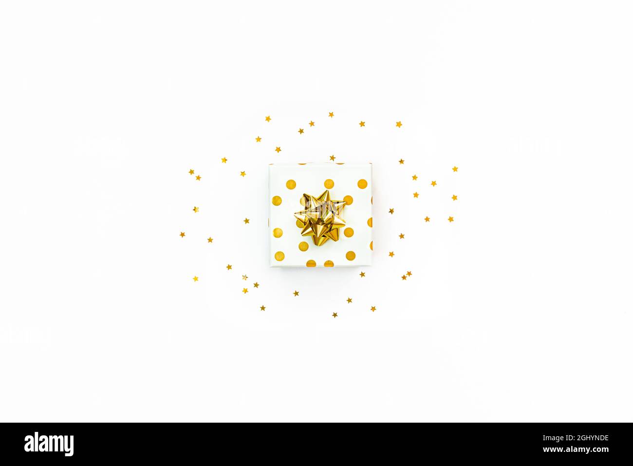 Vue de dessus d'une boîte cadeau à pois dorés et de paillettes dorées en forme d'étoile sur fond blanc. Banque D'Images