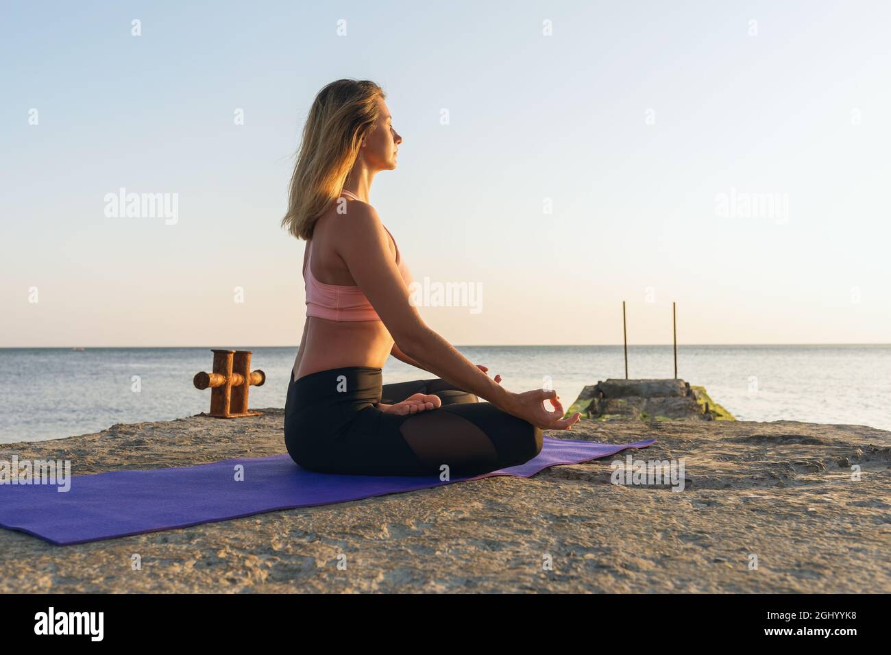 Une femme en vêtements de sport, pratiquant le yoga, assise sur un tapis en position lotus, en soirée sur la mer, est engagée dans la méditation Banque D'Images