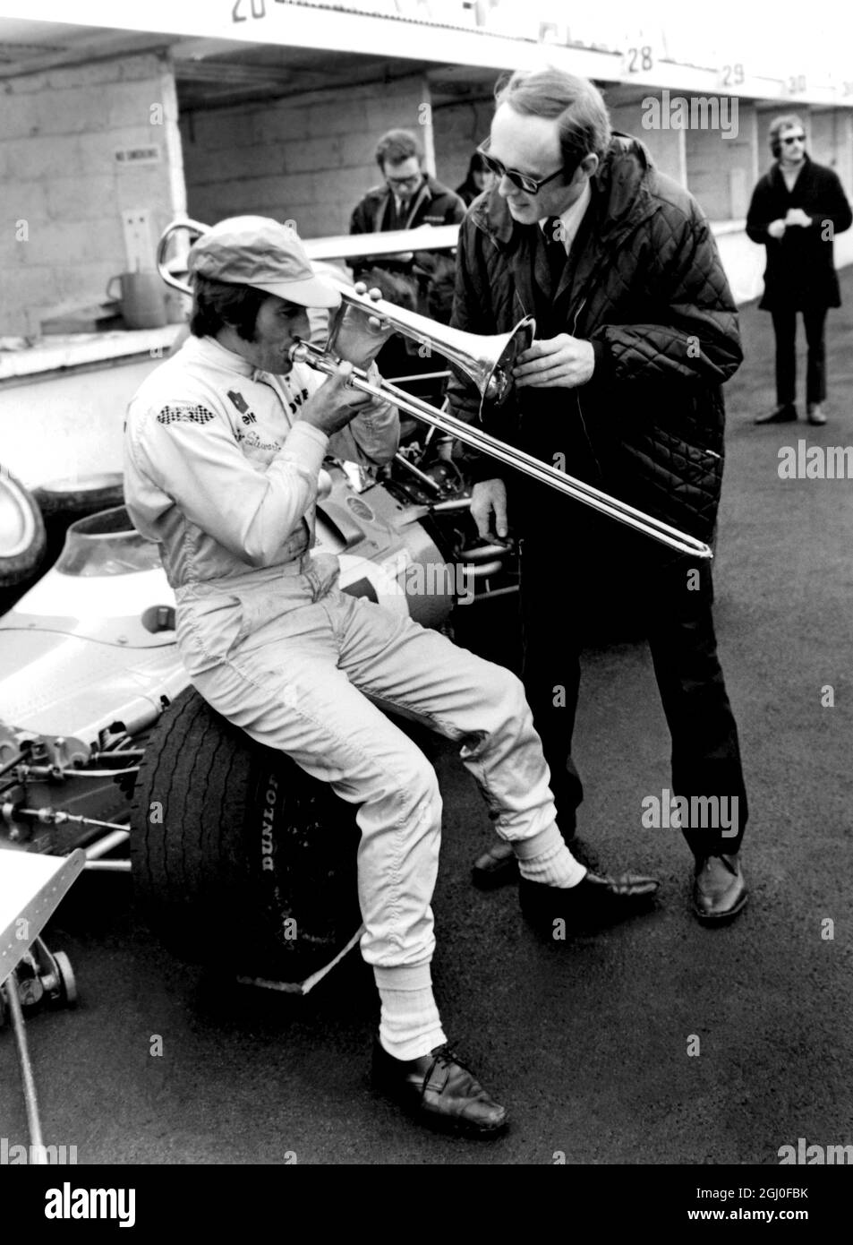 Brands Hatch, Kent: Le pilote de course Jackie Stewart, d'Écosse, ne souffle pas vraiment sa propre trompette - comme vous pouvez le voir - mais le trombone de Chris Barber, le chef du groupe Jazz. Jackie Stewart estime qu'il peut aller plus vite que n'importe quel autre pilote de Grand Prix dans l'eau, et chris affirme qu'il pleut toujours lorsqu'il se présente au circuit de course de Brand Hatch. Ainsi, le jour de la pratique, Chris a obligé Jackie en se retournant, avec l'instrument. Eh bien, il a fait un peu de pluie, mais la pratique a finalement été abandonnée en raison de brouillard épais. Il n'a pas plu hier, mais Jackie a toujours gagné la course des champions dans sa formule 1 C Matra-Ford Banque D'Images