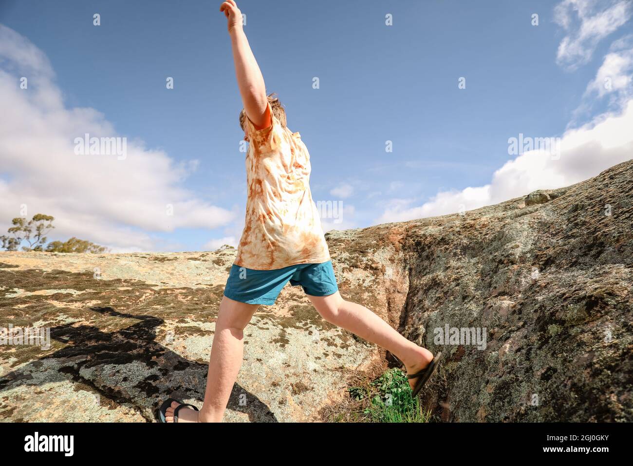 Garçon courant et sautant sur des rochers sous ciel bleu nuageux dans la nature Banque D'Images