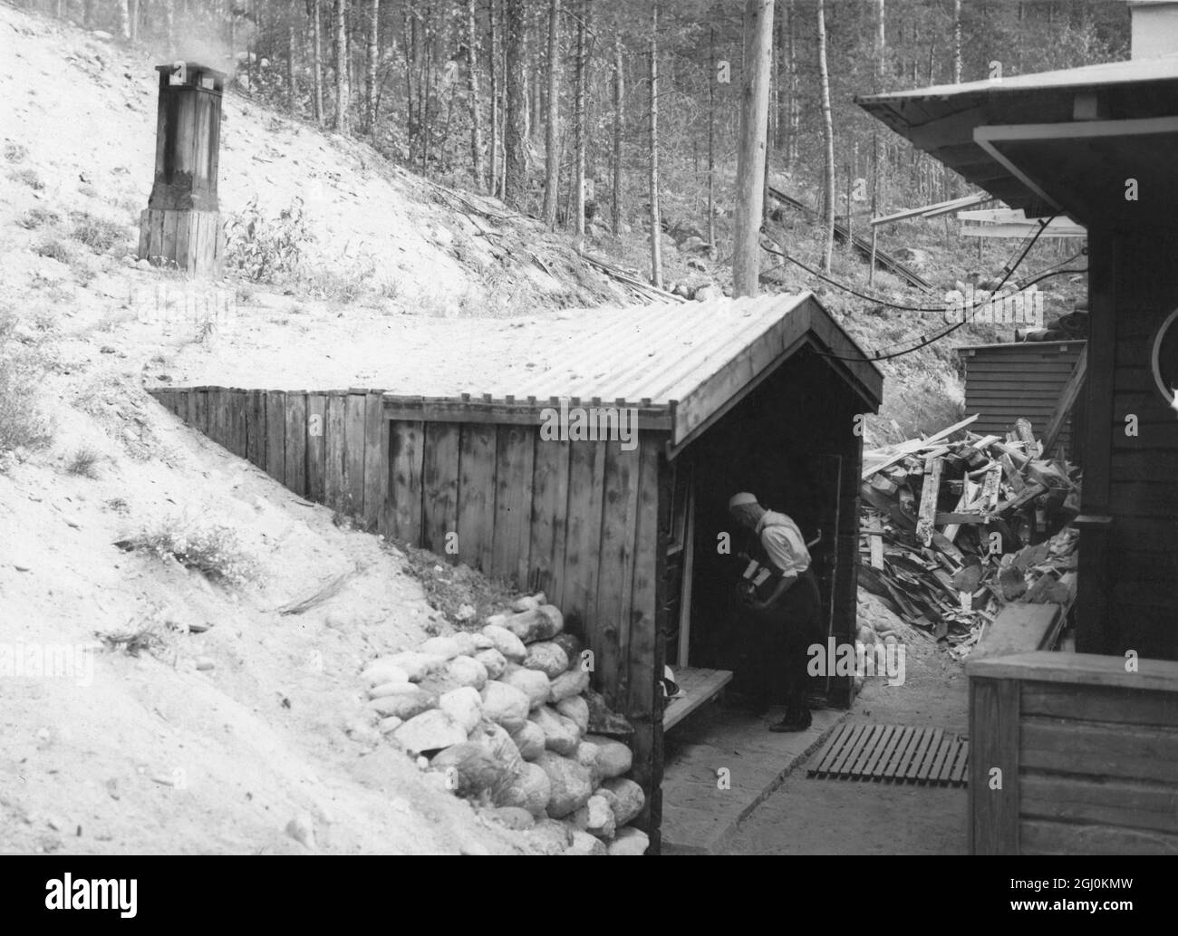 Le Bath House, en partie construit dans la pente de la colline, est une hutte de sauna typiquement finnoise à l'ancienne. Il est construit de bois; la fumée et la vapeur tout au long des années l'ont obscurci. En hiver, la neige profonde couvre le sol tout autour, et les baigneurs, au lieu de plonger dans le lac - qui est gelé - roulent dans la neige. Finlande - années 1930 Banque D'Images