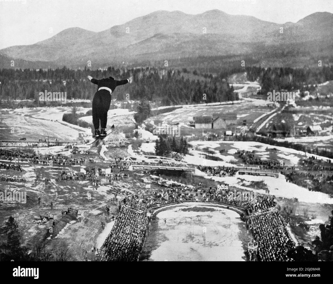 Février 1932: Vue en grand angle du skieur suisse Cesare Chiogna en vol alors qu'il participe à l'épreuve de saut à ski aux Jeux Olympiques, Lake Placid, New York Banque D'Images
