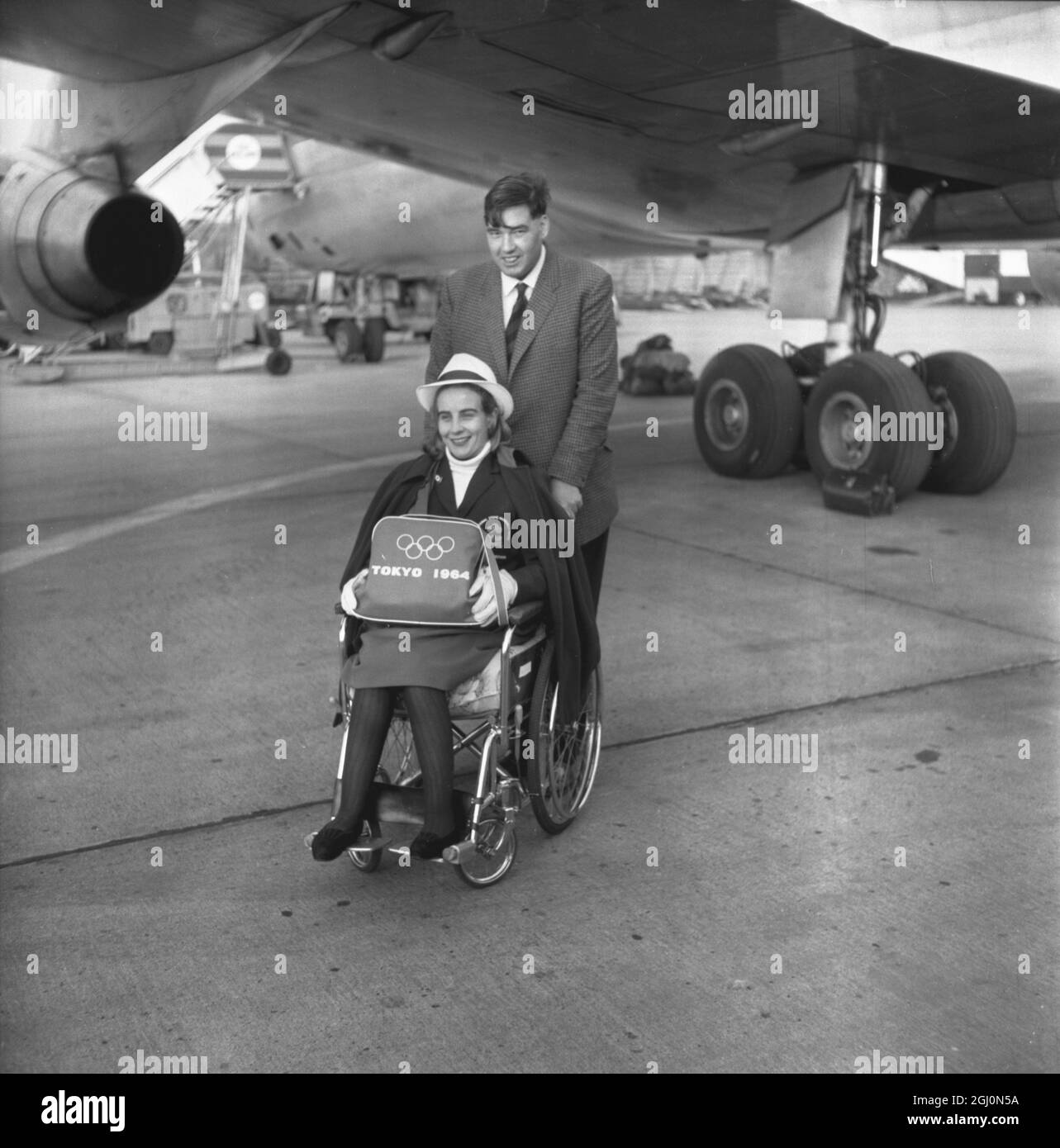 Lord David Masham pousse le fauteuil roulant de sa femme Lady Susan Masham vers son avion à l' aéroport de Londres . Elle participe aux compétitions de natation et de tennis de table des Jeux Paraplegic à Tokyo , au Japon , dans le cadre de l'équipe britannique . 4 novembre 1964 Banque D'Images