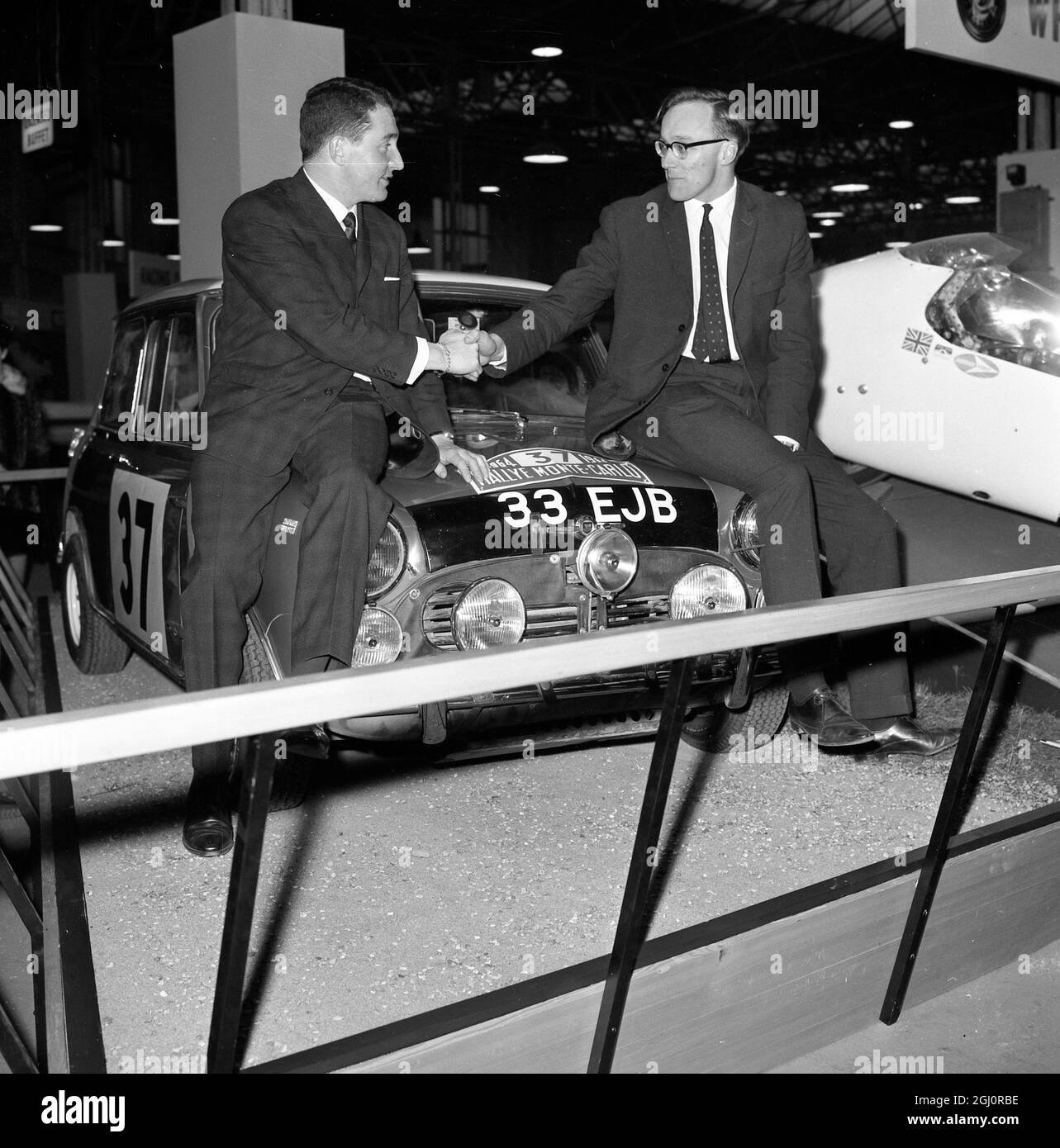 Londres : leurs Morris Cooper se secouent par Paddy Hopkirk (à gauche) et son copilote Henry Liddon (à droite) quand leur voiture est allée sur un stand spécial au Racing car Show à Olympia à Londres aujourd'hui . Les deux ont volé hier après avoir remporté le rallye Monte Carlo 1964 , les premiers Britanniques au faire depuis le 1950 27 janvier 1964 Banque D'Images