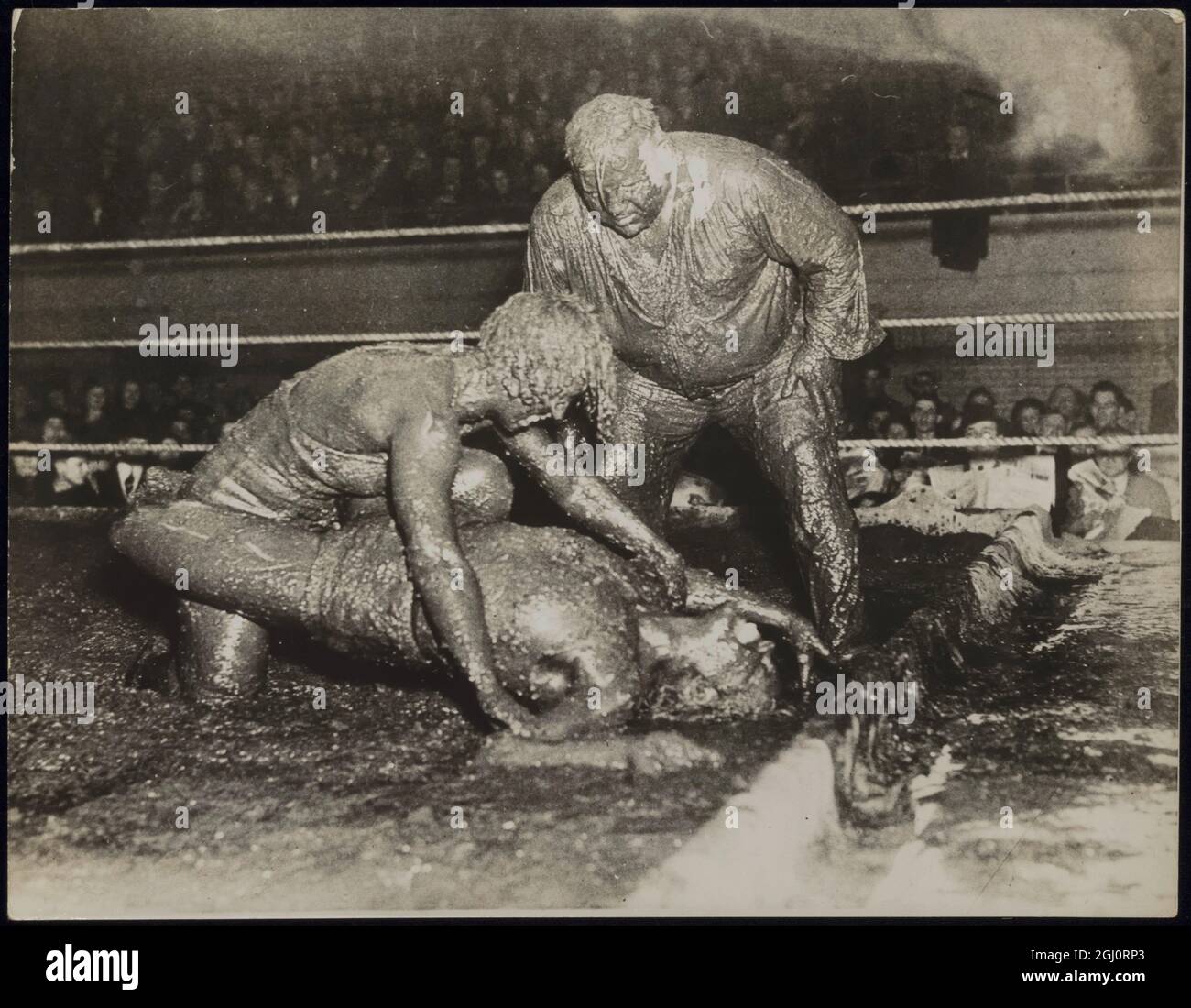 CES FILLES AIMENT L'EXERCICE AVEC LEUR 'MUD PACK'! Mildred (Cyclone) Burke de Kansas City, Missouri, prestataire au championnat du monde de lutte des femmes, End Leona (Babe) Gordon de Chicago s'est donné un sac de boue ''traitement' quand ils ont pris pert dans un match de lutte de style hindou dans un anneau rempli de boue à Akron, Ohio. Mlle Burke a remporté une victoire en une seule chute. PHOTOS MONTRE:- Mildred (Cyclone) Burke (en haut) épingles son adversaire tout aussi boueux, Leone (Babe) Gordon, dans le désordre visqueux comme Ernie Maddock, l'arbitre, est sur le point de taper Miss Burke sur l'épaule pour la déclarer la gagnante. L'arbitre Banque D'Images