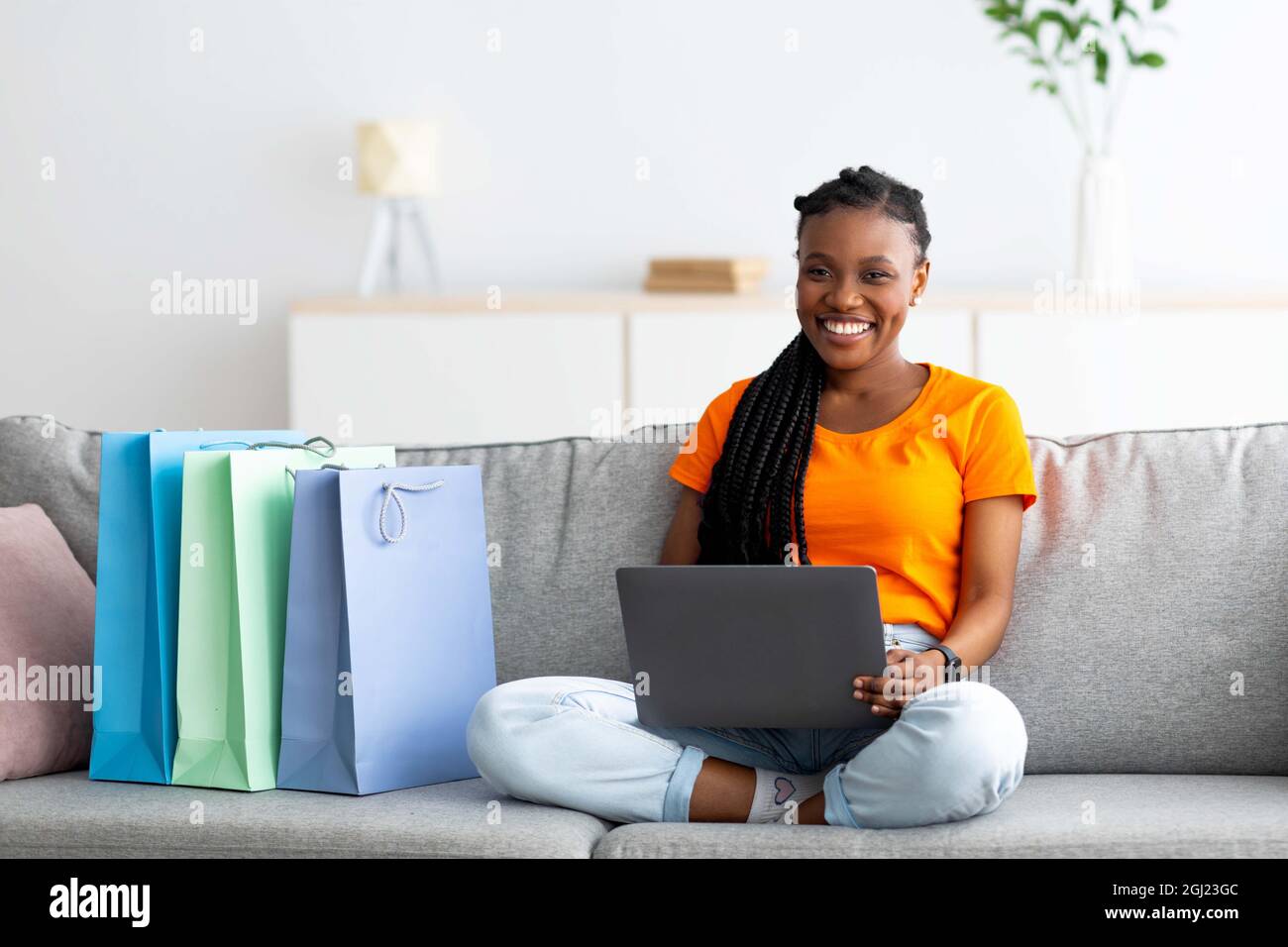 Concept de shopping à domicile. Jolie femme américaine africaine avec carte  de crédit et ordinateur portable achetant des marchandises en ligne dans la  boutique Internet, assis sur le canapé avec le client