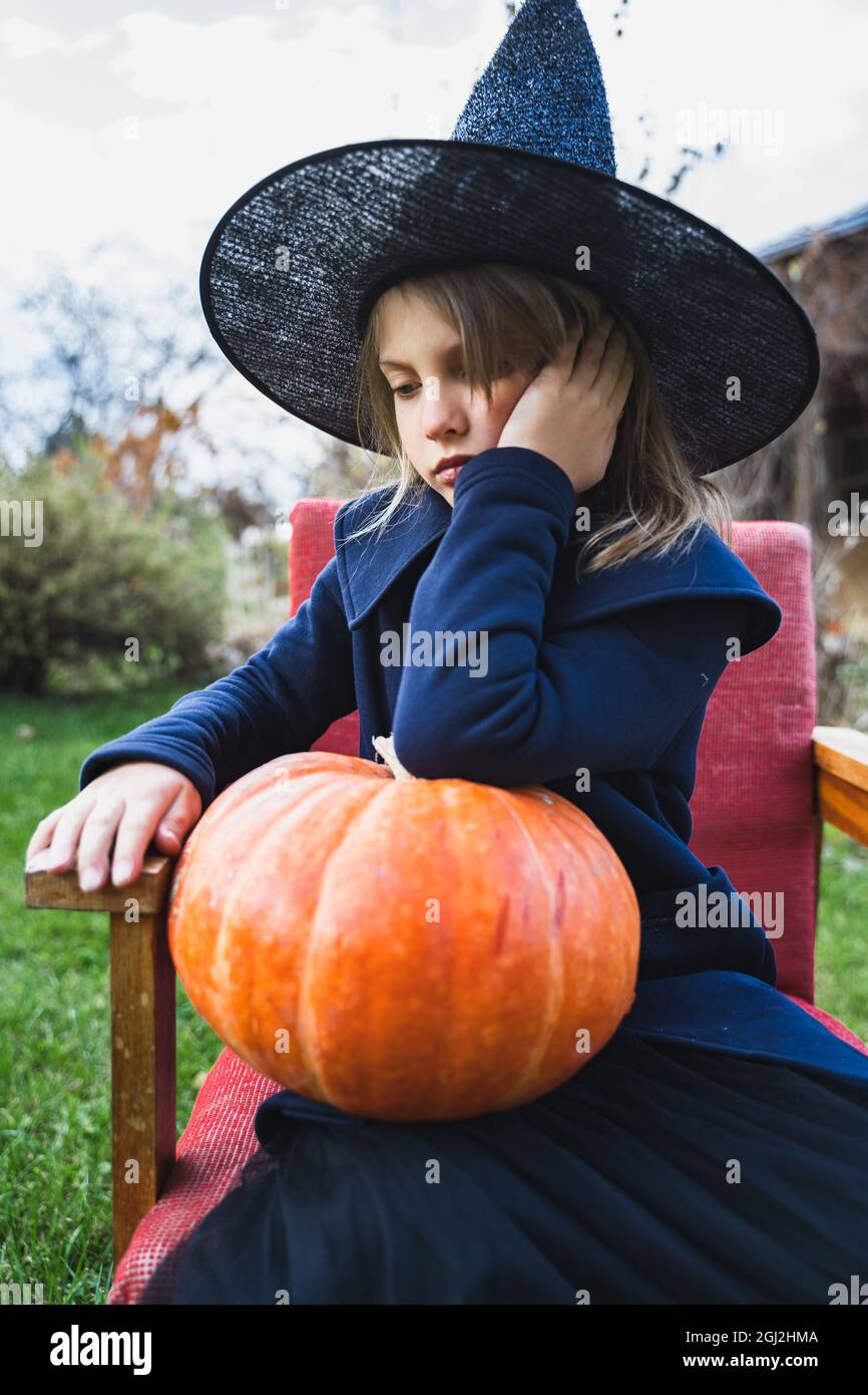 Petite fille effrayante en costume de sorcière, chapeau avec grande  citrouille célébrant les vacances d'halloween. Assis sur un fauteuil,  manteau de citrouille. Image élégante. Horro Photo Stock - Alamy