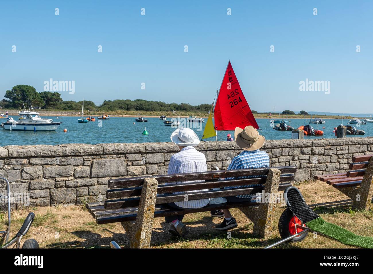 Couple senior assis sur un banc d'observation des bateaux et des dinghies naviguant à Keyhaven, Hampshire, Angleterre, Royaume-Uni Banque D'Images