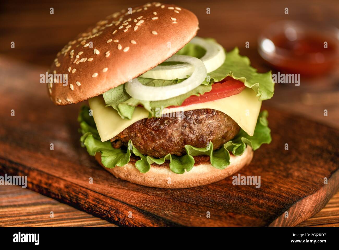 Hamburger de bœuf maison avec fromage, tomate et salade sur fond de bois. Banque D'Images