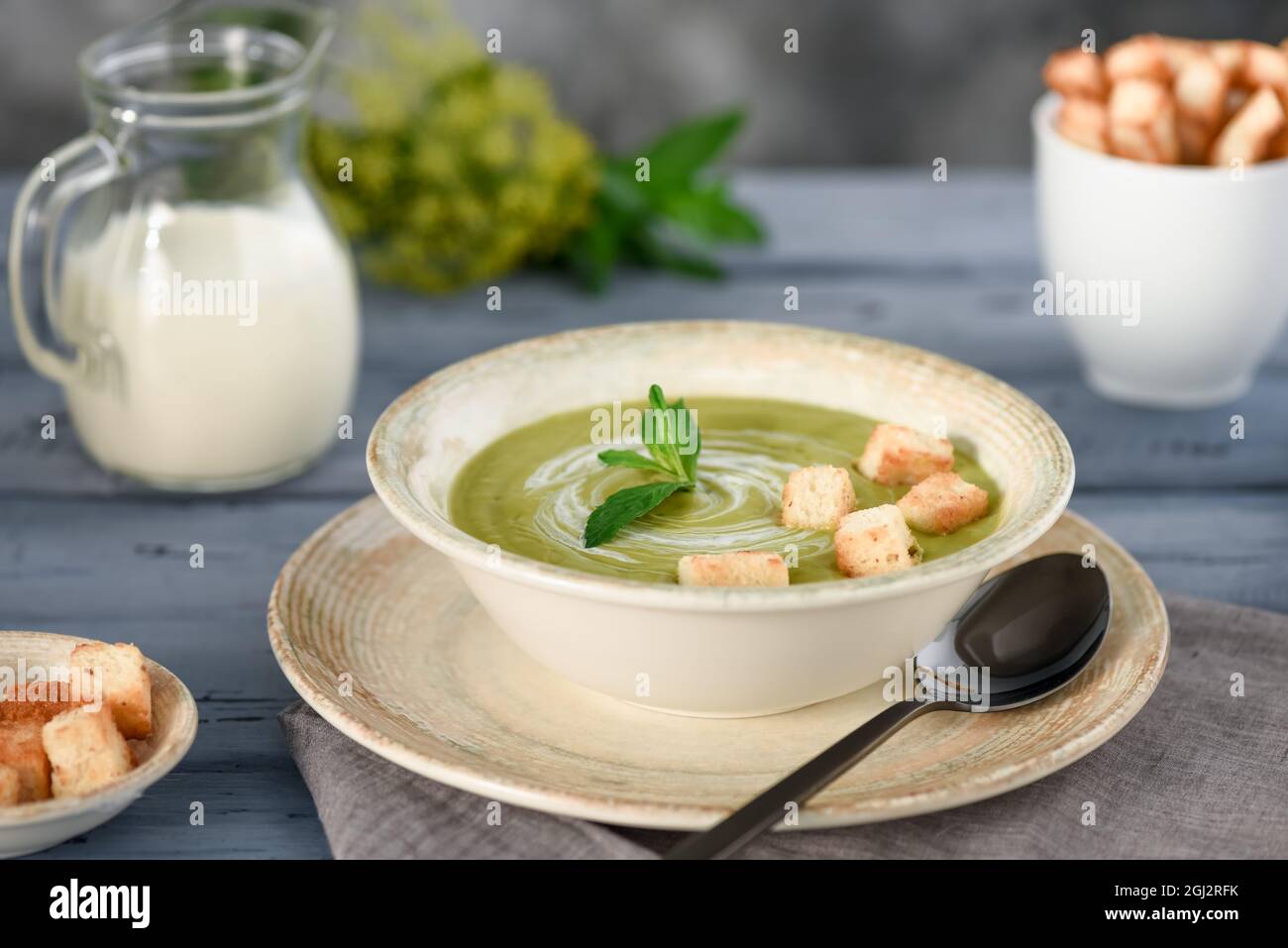 Soupe à la crème de brocoli avec des croûtons et des feuilles de menthe. Versé avec de la crème. La crème est versée dans une verseuse en verre. L'arrière-plan est flou. Banque D'Images