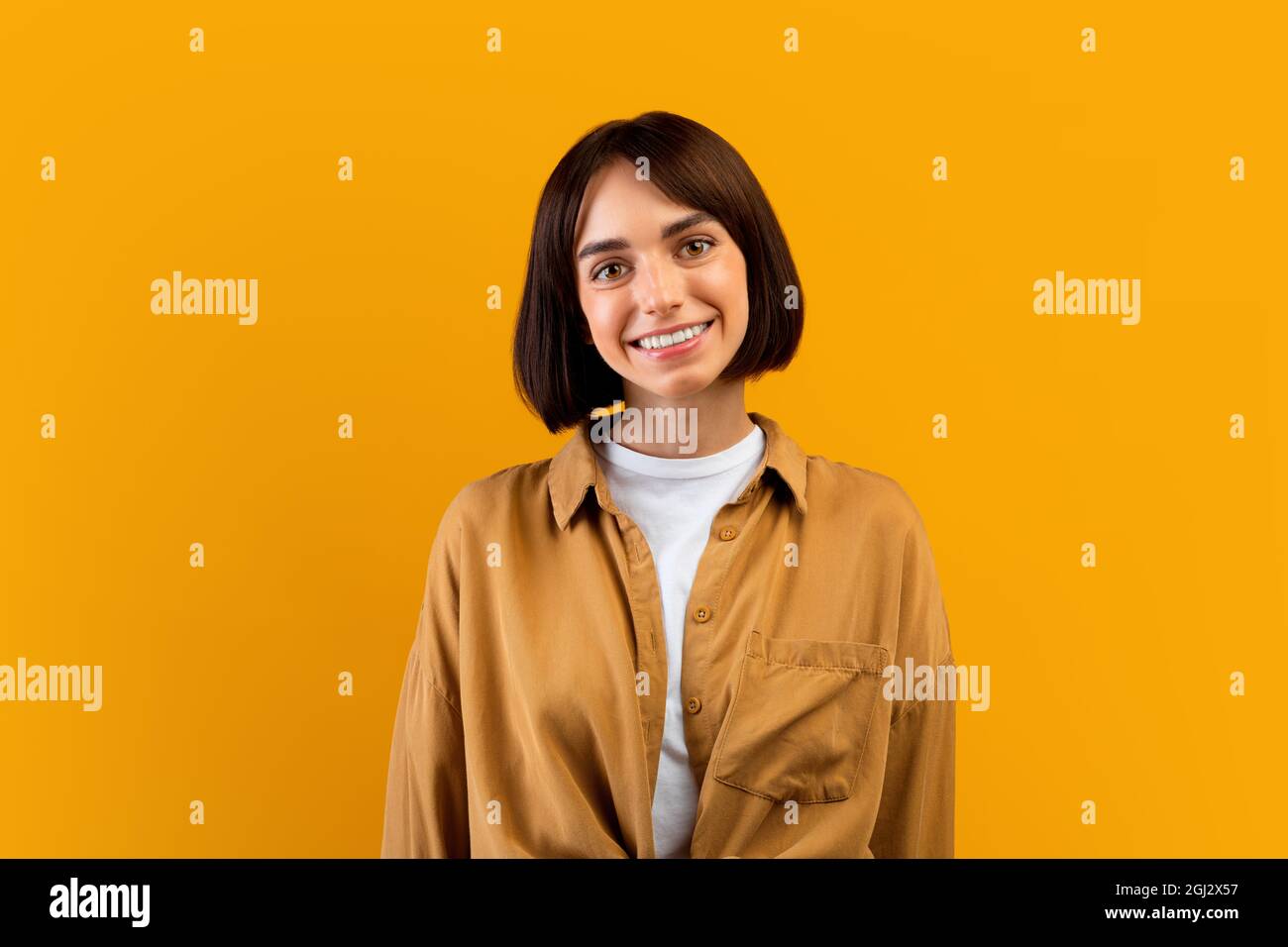 Personne heureuse. Portrait de femme souriante avec bob coupe de cheveux regardant l'appareil photo, posant en studio, isolé sur fond jaune, gros plan tourné avec copie s. Banque D'Images