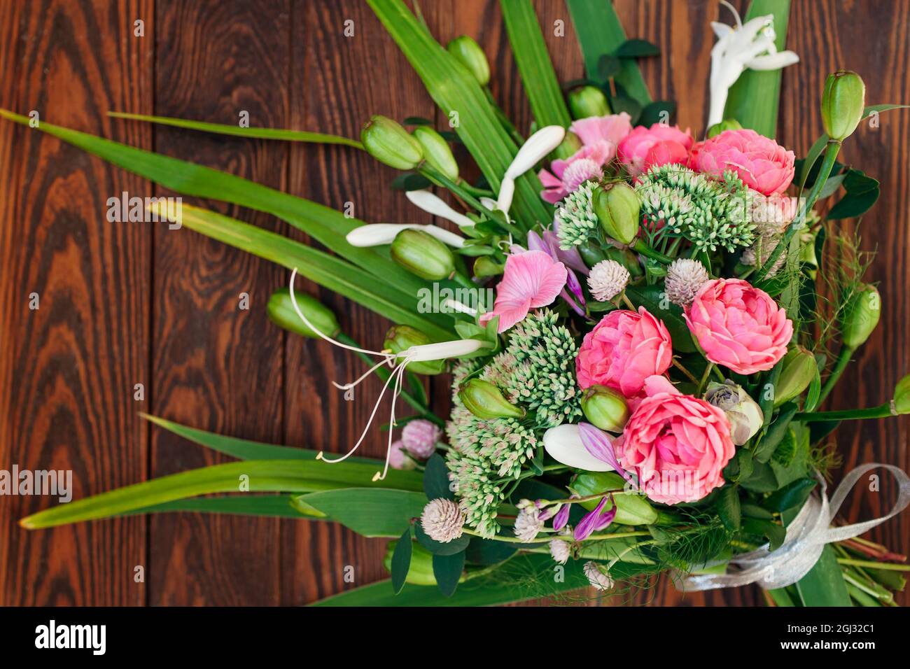 Bouquet de fleurs roses blanches vertes disposées sur fond de bois. Roses, sedum, hosta, gousses de graines, gomphrena et graminées Banque D'Images