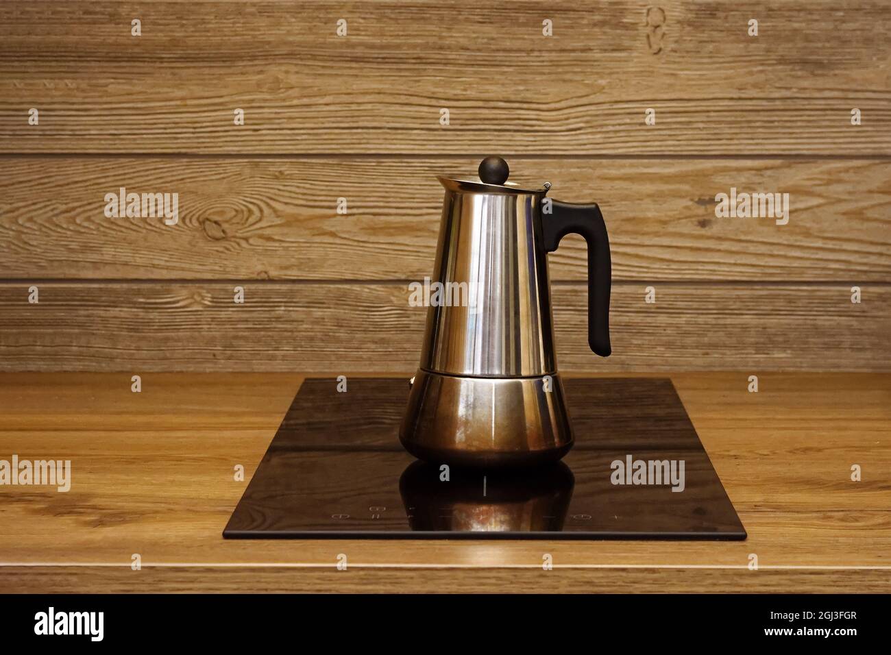 Geyser machine à café sur le panneau de chauffage électrique de la cuisinière sur le fond d'un mur en bois. Banque D'Images