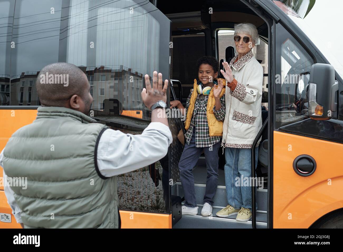 Un garçon noir souriant embrassé par une grand-mère qui agite la main tout en disant Au revoir au père, ils se mettent en bus Banque D'Images