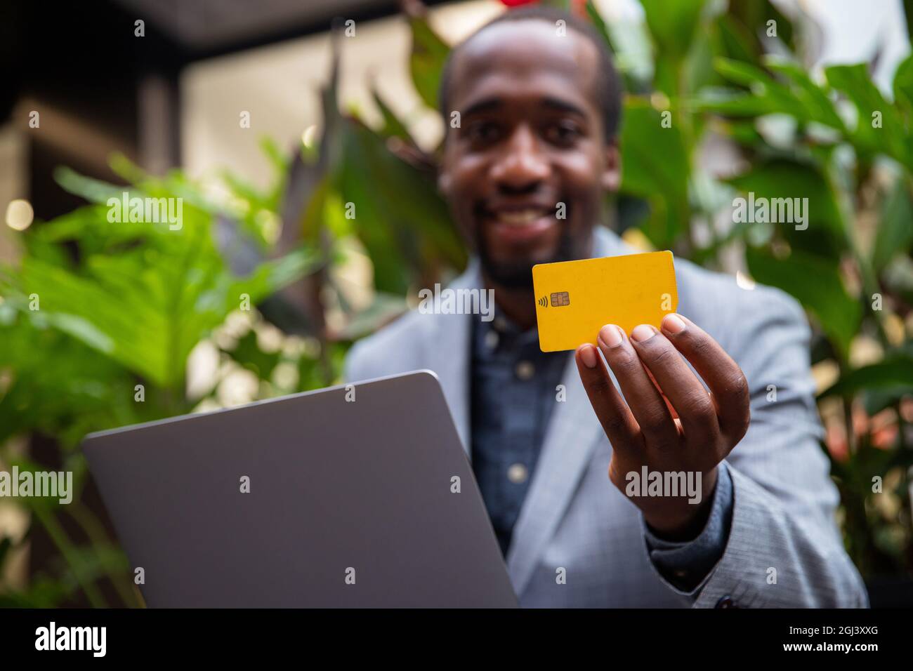 L'homme d'affaires africain est titulaire d'une carte de crédit et fait un achat en ligne avec son ordinateur portable. Souriant et élégant homme millénaire - homme technologique buyi Banque D'Images