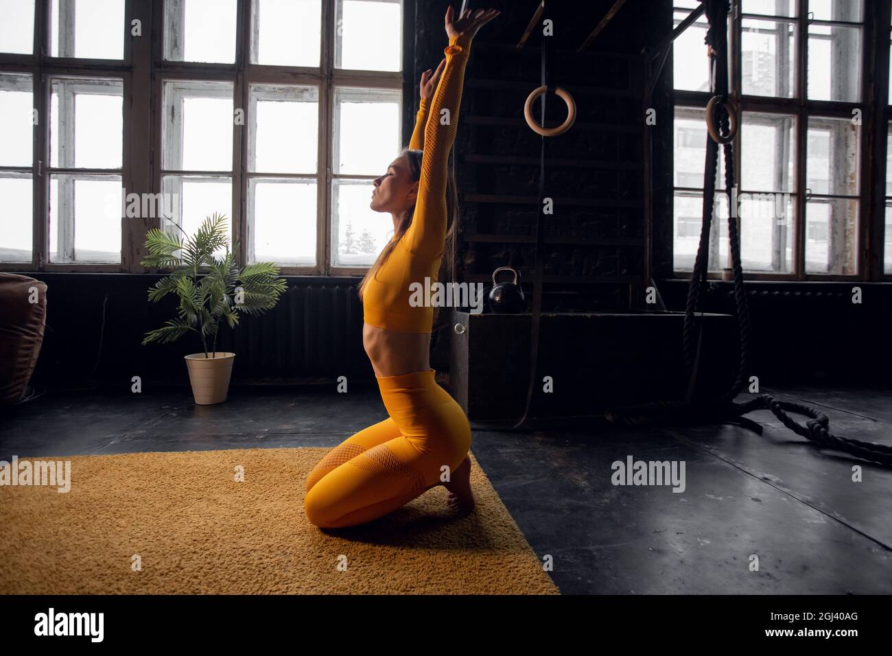 Jeune femme yogi pratiquant le concept de yoga, faisant un exercice King Pigeon à pattes, s'entraîner, portant des vêtements de sport, arrière-plan de studio loft Banque D'Images