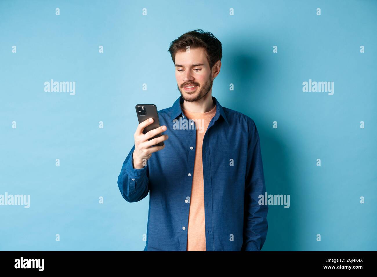 Beau homme moderne utilisant le téléphone mobile, lisant l'écran de  smartphone et souriant, la mise en réseau sur fond bleu Photo Stock - Alamy