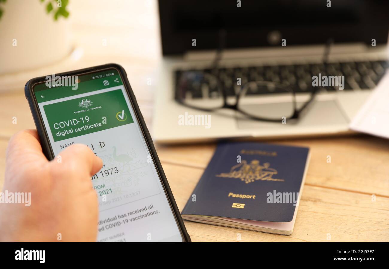 Preuve numérique officielle du certificat de vaccination Covid-19 du gouvernement australien sur un téléphone portable. Passeport flou en arrière-plan et ordinateur portable Banque D'Images