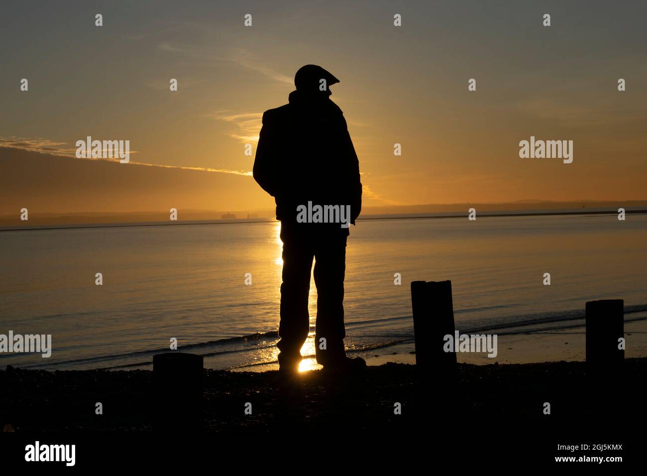 Un homme regarde le soleil se coucher sur le Solent à Hayling Island, Hampshire Royaume-Uni Banque D'Images