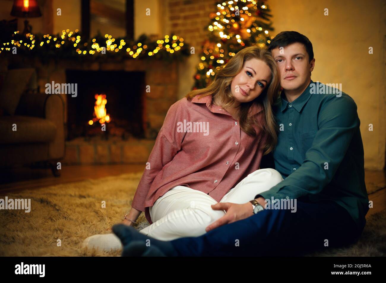Beau couple caucasien d'âge moyen posant à l'intérieur de noël avec un arbre de noël et des guirlandes. Mise au point douce sélective, effet de grain de film Banque D'Images