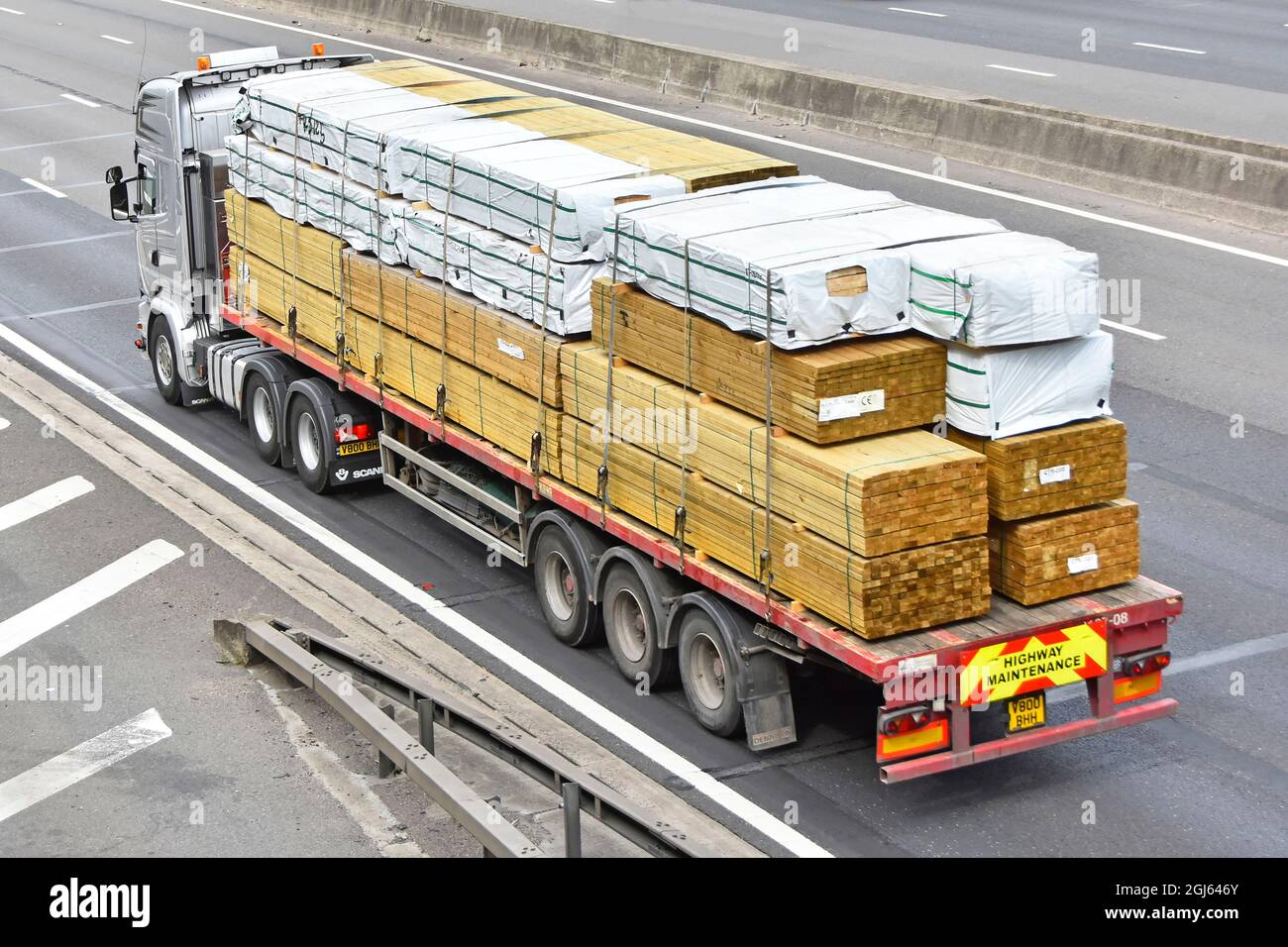 Vue aérienne latérale arrière d'un camion et d'une remorque articulée chargés de matériaux de construction en bois, certains enveloppés dans du plastique anglais Banque D'Images