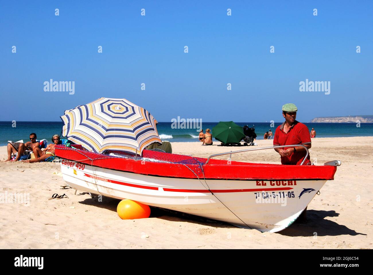 Espagnol homme debout près de son traditionnel bateau de pêche en bois rouge et blanc sur la plage avec touriste profitant du soleil, Zahara de los Atunes, Espagne Banque D'Images