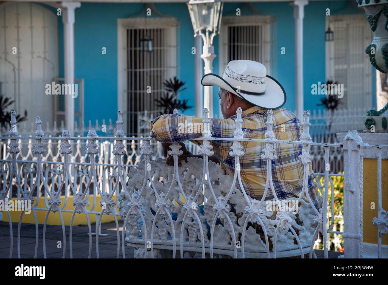 Homme avec chapeau de cow-boy assis sur un banc en fer forgé à Trinidad, Cuba Banque D'Images