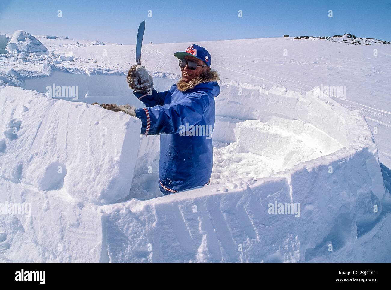 Baker Lake, Nunavut, Canada. Homme aîné inuit, habillé de vêtements modernes de l'arctique, construisant des igloo en sculptant des blocs de neige et en les plaçant soigneusement. THI Banque D'Images