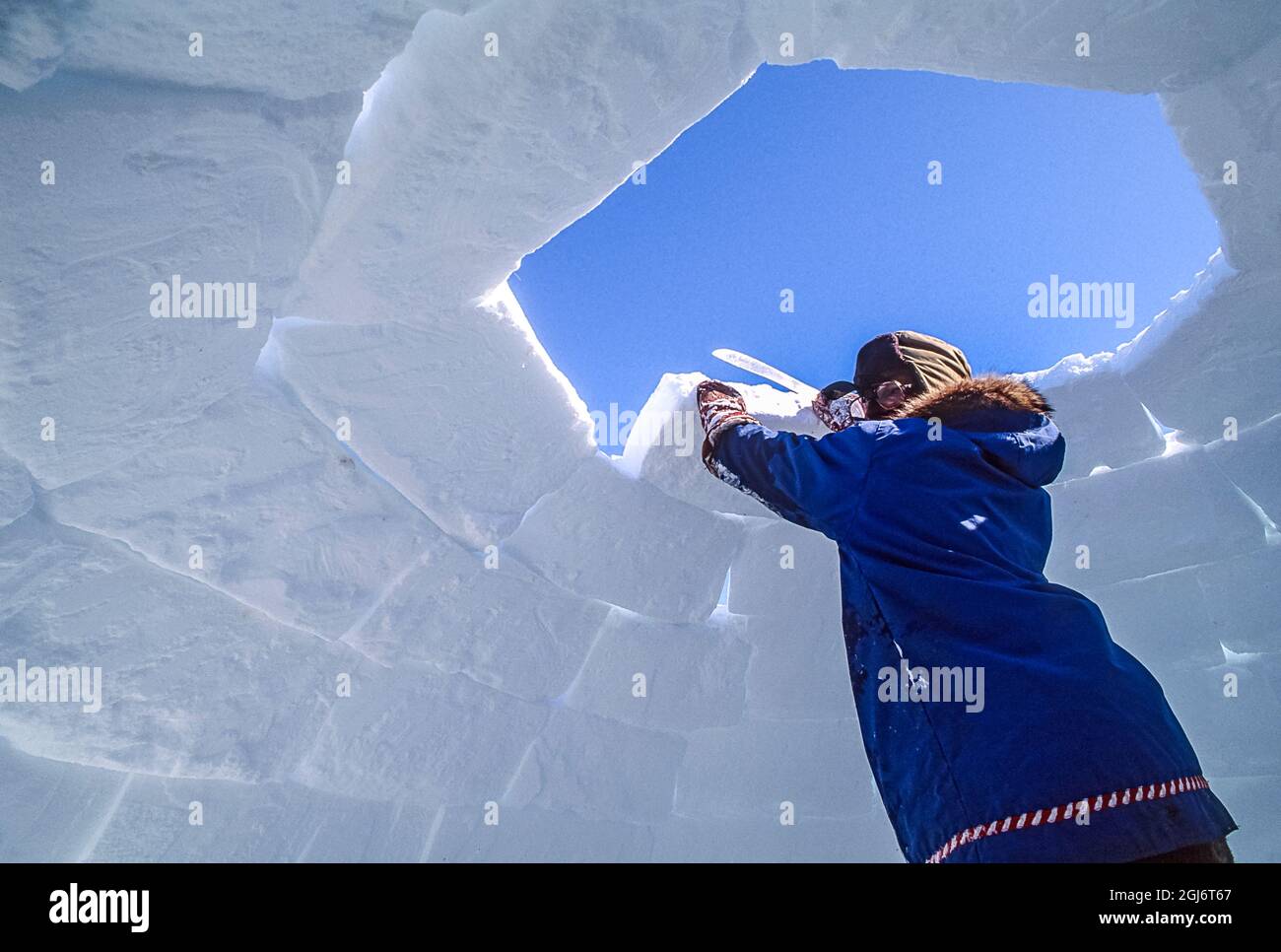Baker Lake, Nunavut, Canada. Homme aîné inuit, habillé de vêtements modernes de l'arctique, construisant des igloo en sculptant des blocs de neige et en les plaçant soigneusement. THI Banque D'Images