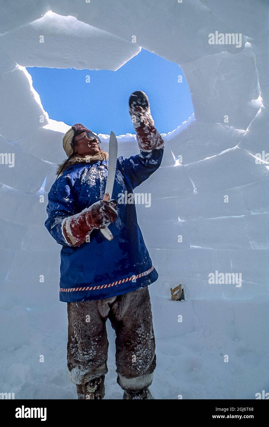 Baker Lake, Nunavut, Canada. Homme aîné inuit, habillé de vêtements modernes de l'arctique, construisant des igloo en sculptant des blocs de neige et en les plaçant soigneusement. THI Banque D'Images