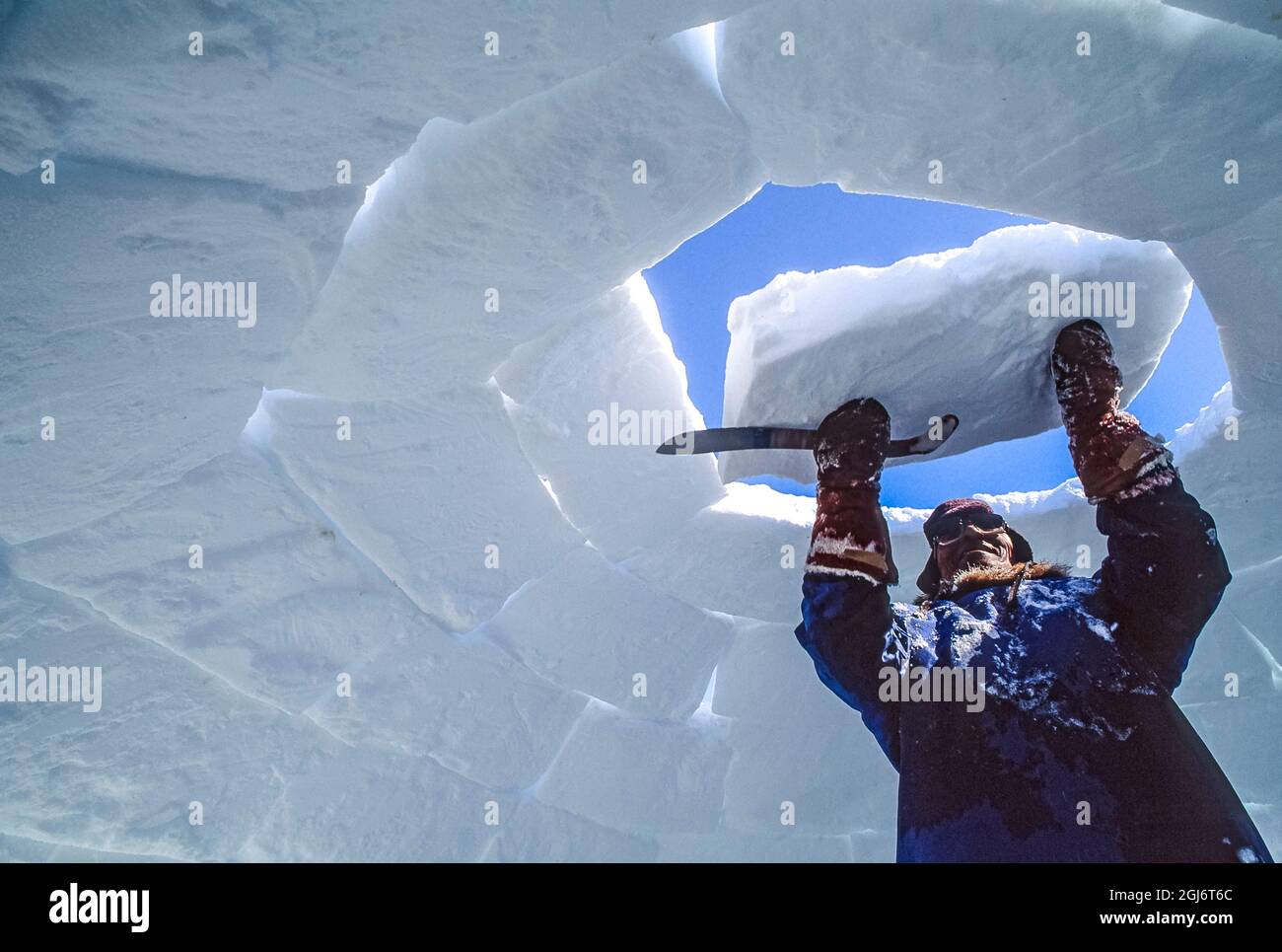 Baker Lake, Nunavut, Canada. Homme aîné inuit, habillé de vêtements modernes de l'arctique, construisant des igloo en sculptant des blocs de neige et en les plaçant soigneusement. THI Banque D'Images