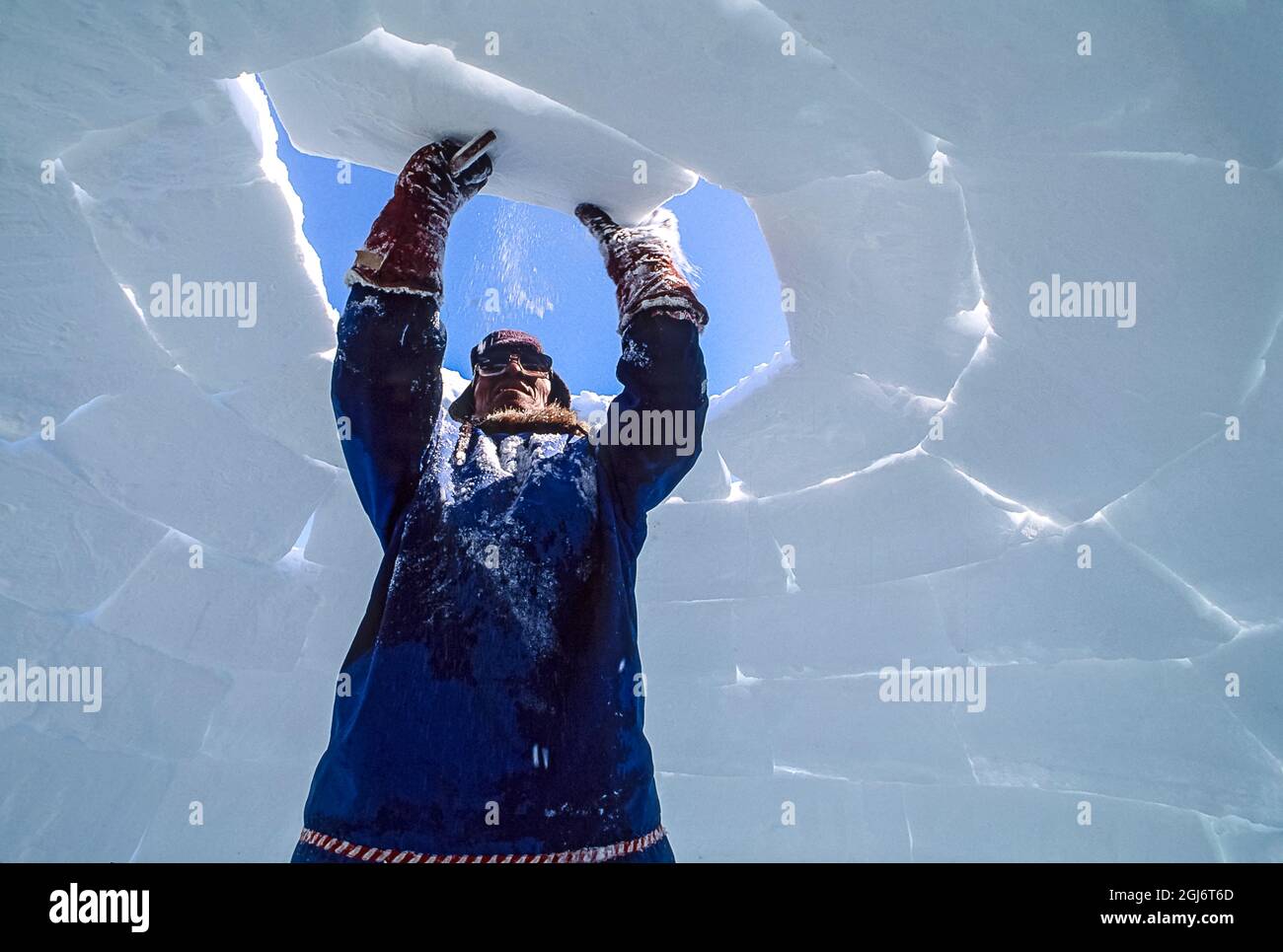 Baker Lake, Nunavut, Canada. Homme aîné inuit, habillé de vêtements modernes de l'arctique, construisant des igloo en sculptant des blocs de neige et en les plaçant soigneusement. THI Banque D'Images