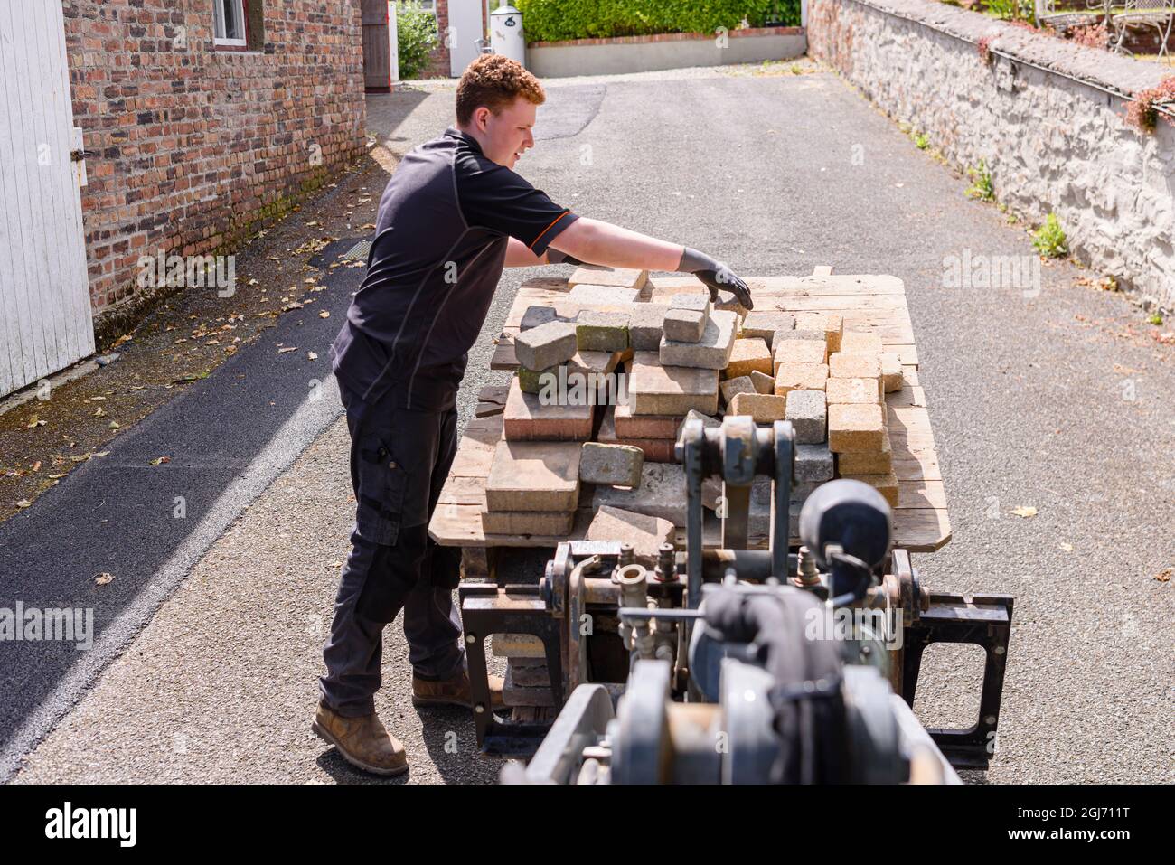 Un jeune homme arrange les pavés de briques sur une palette lorsqu'il est soulevé par un chargeur élévateur. Banque D'Images