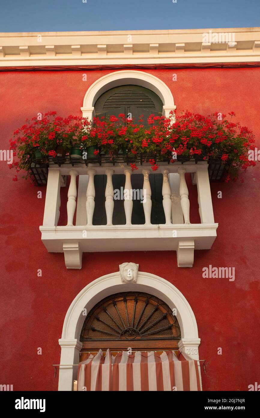 Italie, Burano. Bâtiments rouges et géraniums sur balcon. Banque D'Images