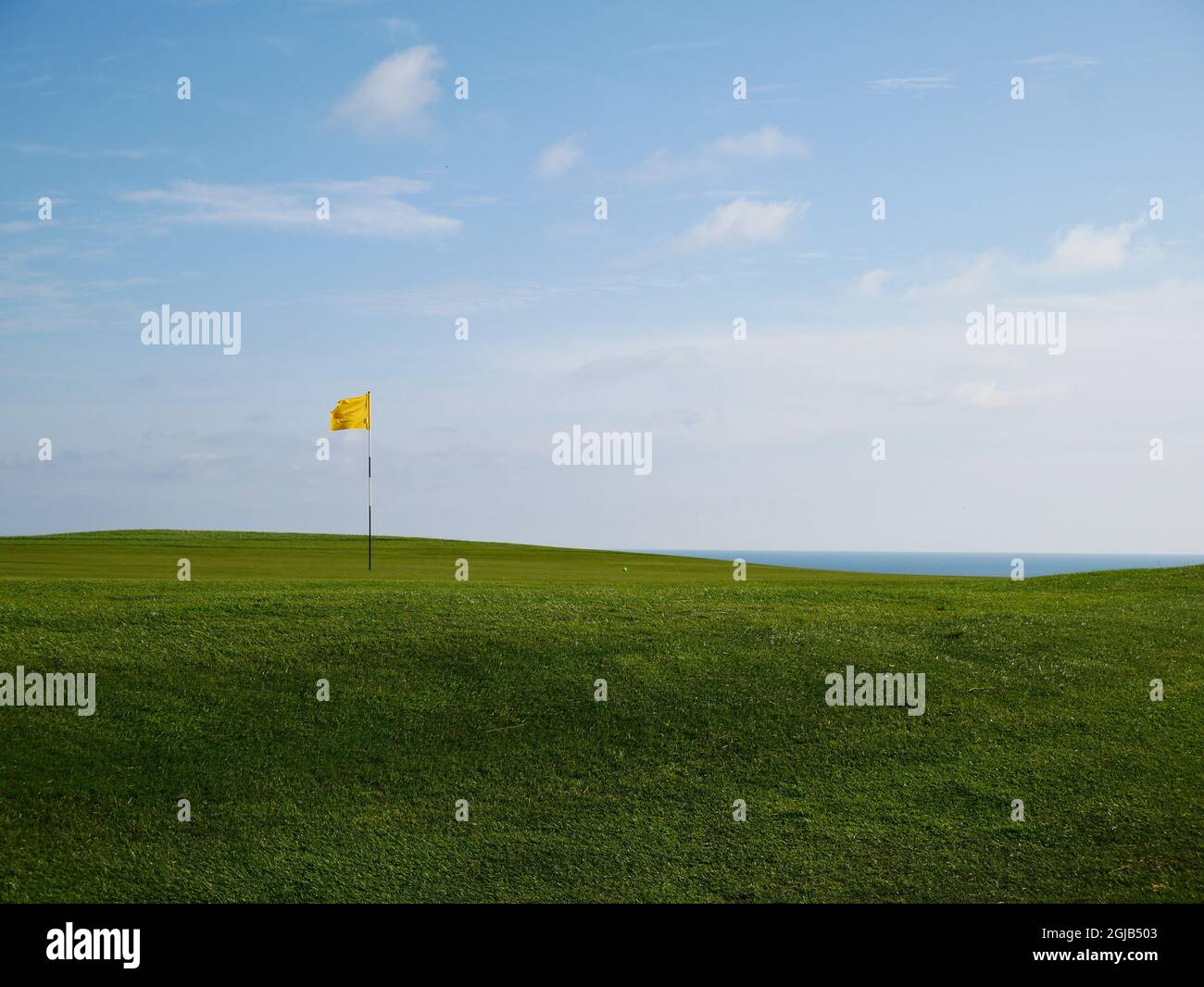 Drapeau jaune marquant la position du trou sur un green sur un parcours de golf côtier. Banque D'Images