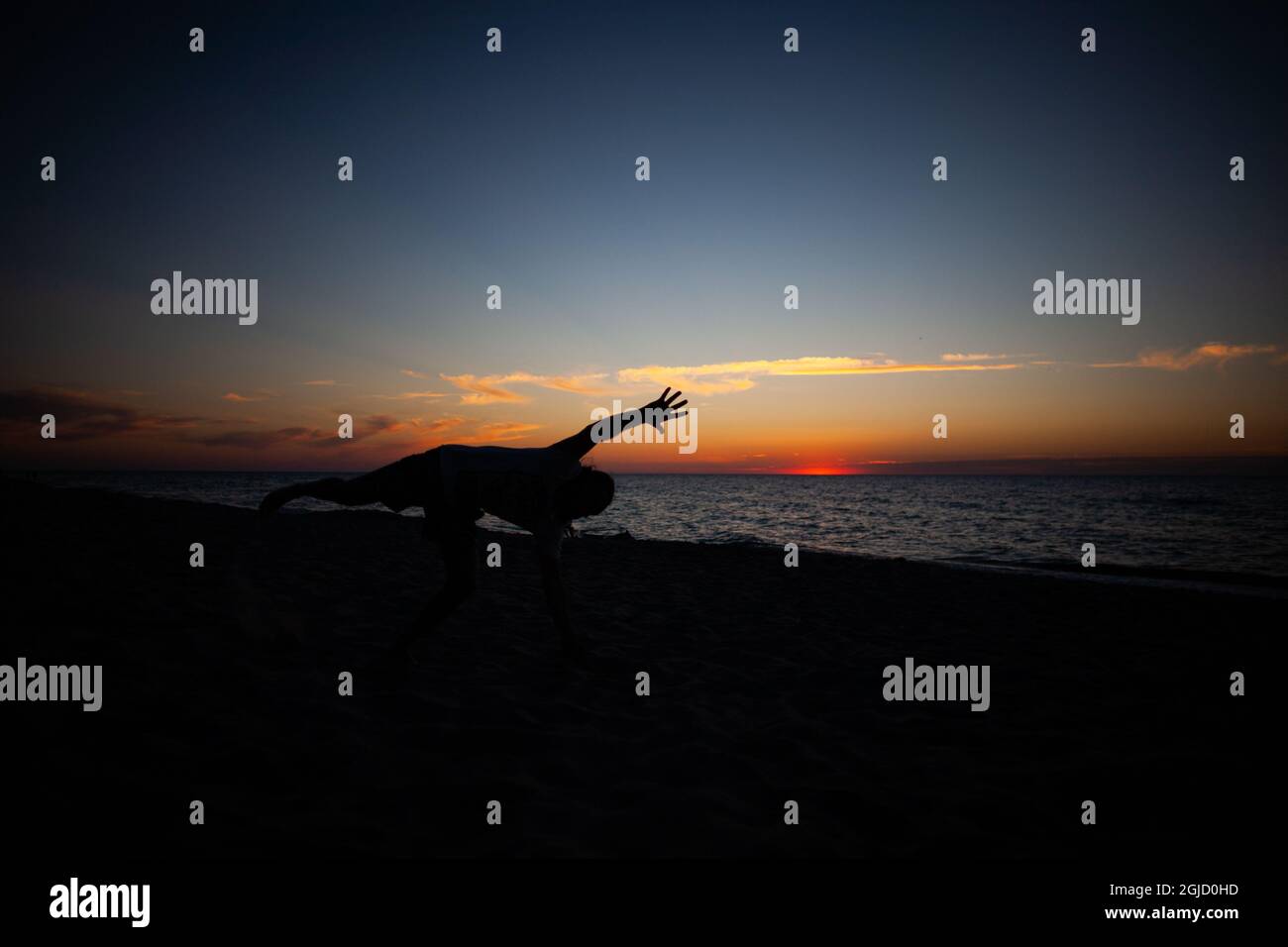 Silhouette d'un homme qui fait de l'exercice sur une roue à cardans sur la plage au coucher du soleil avec la mer et le ciel en arrière-plan Banque D'Images