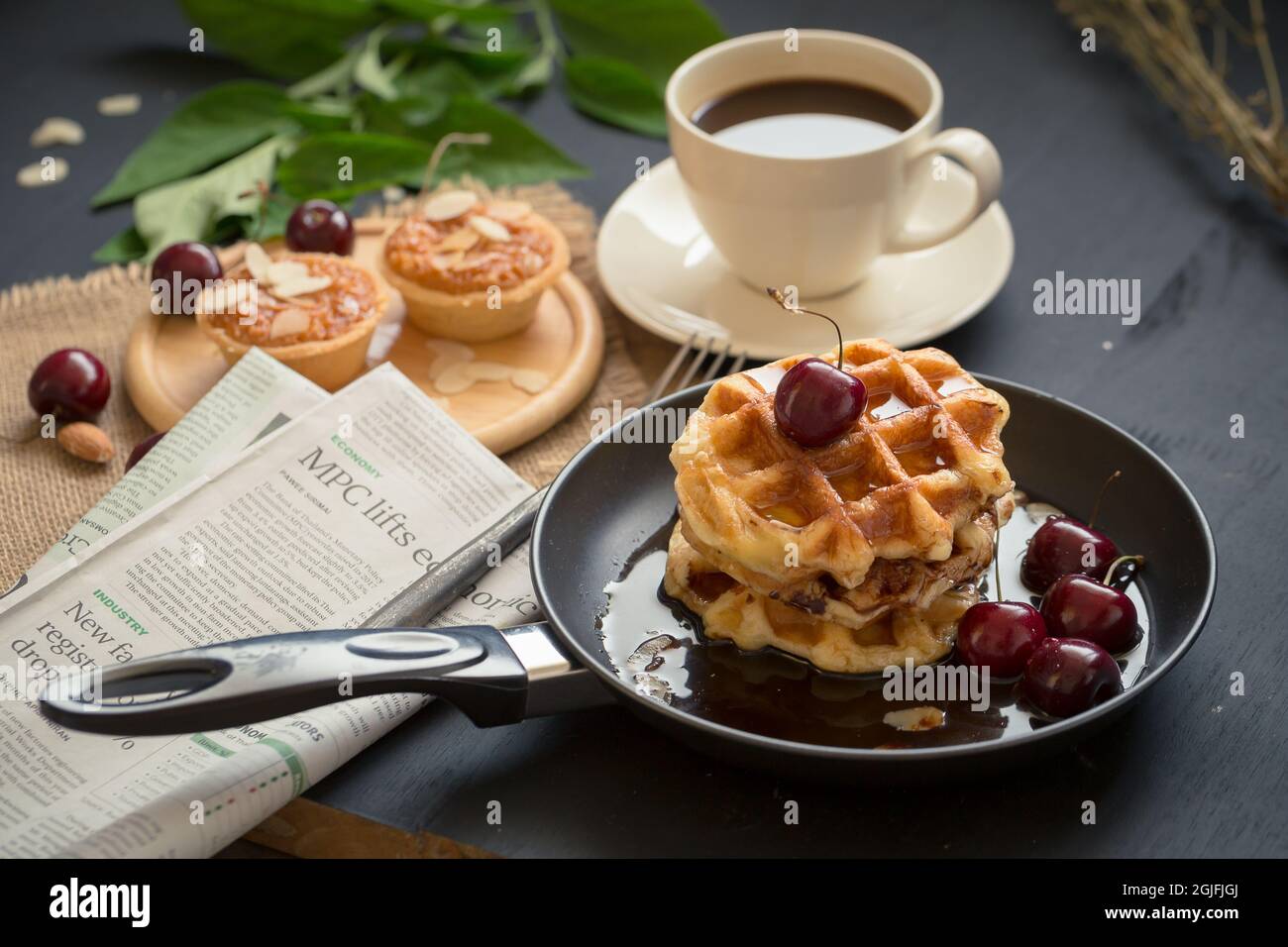 Concept de petit-déjeuner avec boisson au café. Inclut des tartes croustillantes aux amandes, des gaufres et des cerises fraîches. Banque D'Images