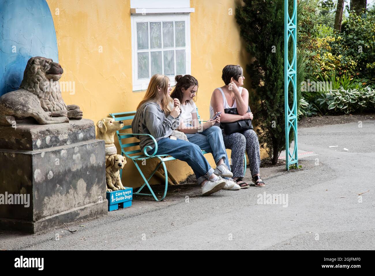 Trois filles assises sur un banc de métal à Portmerion, dans le nord du pays de Galles, au soleil, isolées et préoccupées par les téléphones mobiles et les pensées Banque D'Images